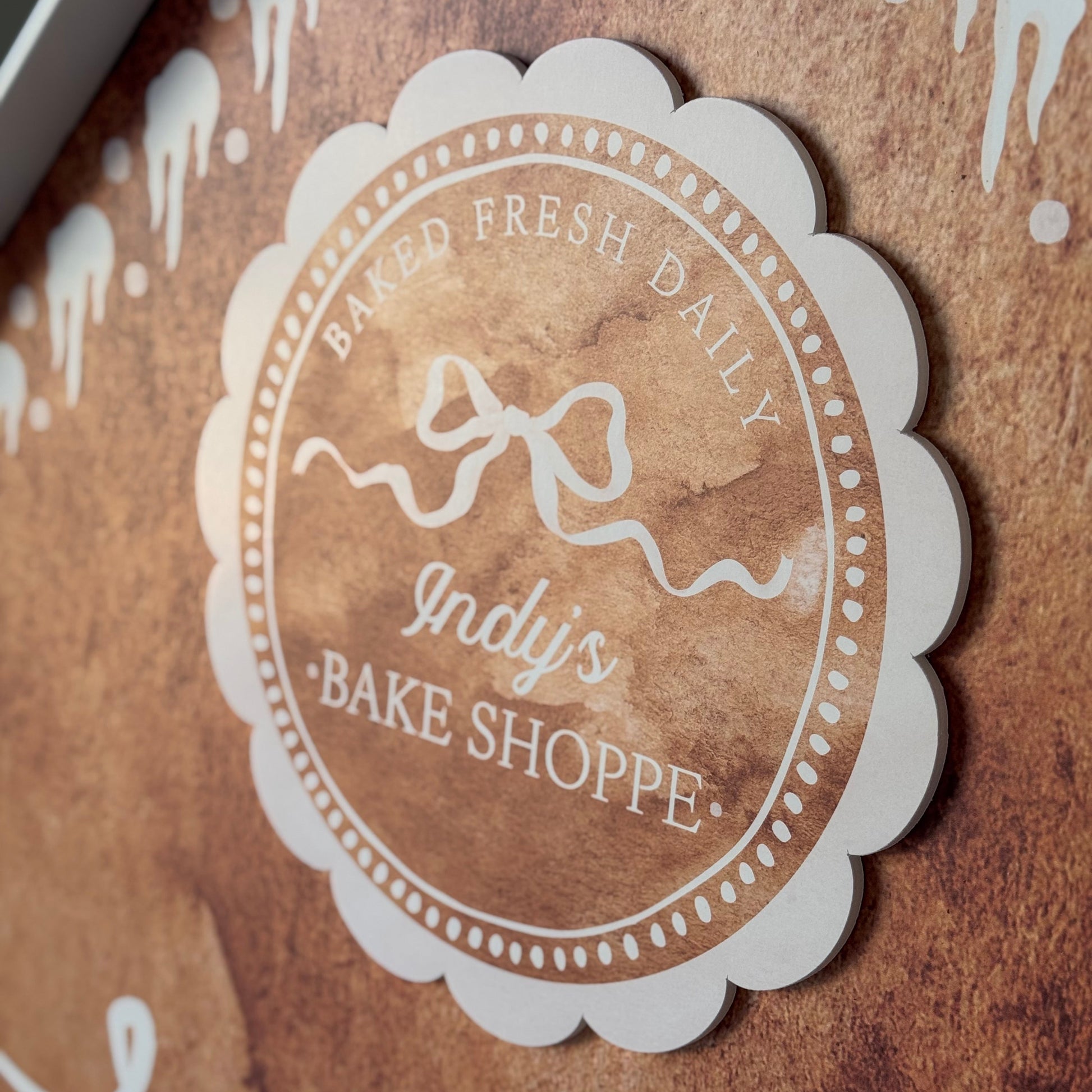 Logo of Indy's Bake Shoppe on a brown background with white decorative elements.
