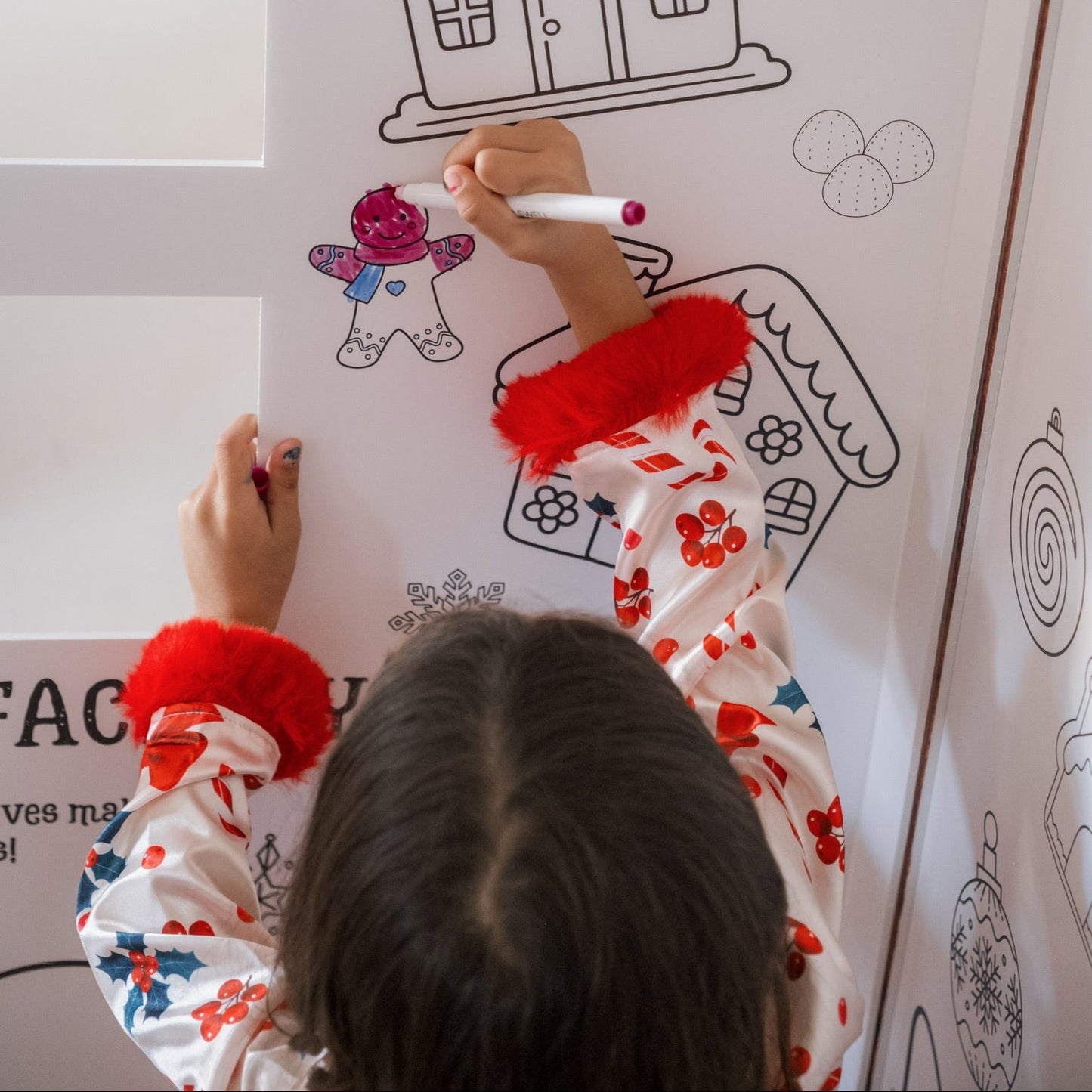 Child coloring a gingerbread house on a large coloring sheet with other Christmas-themed illustrations.